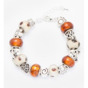 The Bronze Tabby Bracelet features a silver chain with an adjustable clasp, adorned with alternating amber-colored and cream-colored beads. It also includes silver decorative charms such as spiral designs, paw prints, and intricate knot patterns. Touches of bronze add a unique flair to this exquisite piece.