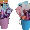 Two Automotive Baskets, one pink and one blue, containing beauty products. Items include Sweet Pea hand sanitizer, iridescent nail polish, blush, a face mask, and a pair of scissors. The baskets are filled to the brim with neatly arranged cosmetics and accessories.