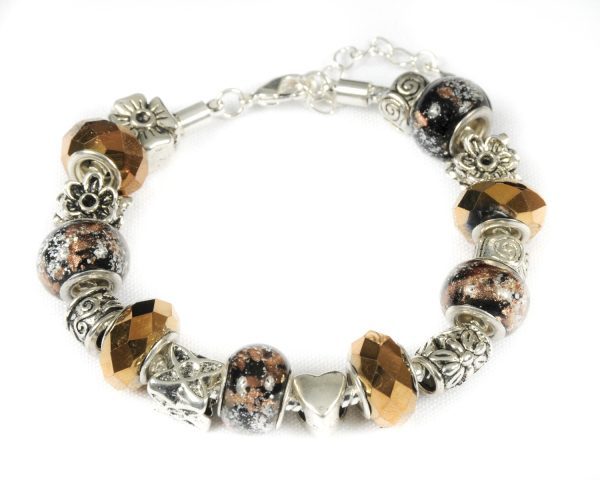 Introducing the Bronze Beauty Bracelet: a stunning silver charm bracelet adorned with a variety of exquisite beads and charms. The bracelet showcases faceted bronze-colored beads, glittery black and copper speckled pieces, and intricate floral silver ornaments. Charms include captivating designs such as a star, a heart, and beautiful floral motifs, all elegantly set against a white backdrop.