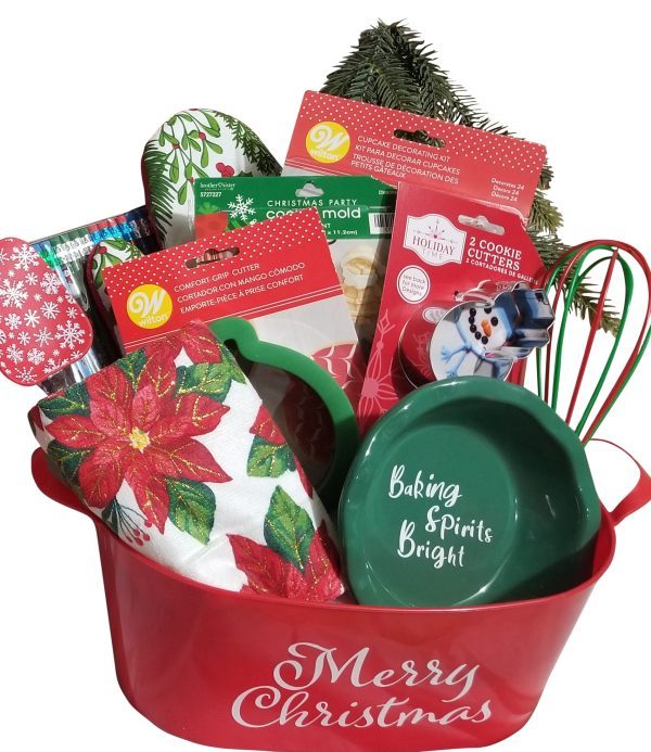 A festive red Automotive Basket labeled "Merry Christmas" holds a holiday-themed assortment, much like a cheerful basket. Inside, you'll find a poinsettia-patterned towel, cookie cutters, cupcake cups, a red and green whisk, holiday paper plates, and a green bowl with "Baking Spirits Bright" written on it.