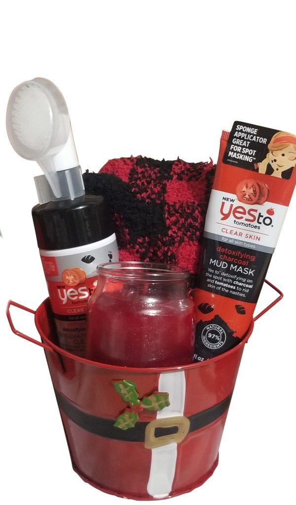 The Automotive Basket, adorned with a festive Santa outfit design, contains a face mask applicator, a bottle of facial cleanser, a tube of detoxifying mud mask, a red and black knitted cloth, and a red jar candle.