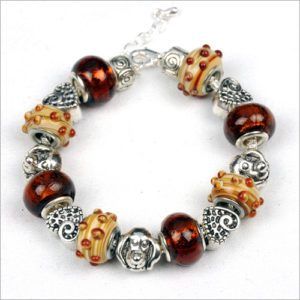 The Dog's Day Out Bracelet is perfect for any canine-themed event, featuring a beautiful mix of brown and beige beads adorned with red dot accents. This charming piece also includes intricately detailed silver beads with floral and spiral designs. The bracelet is finished with a secure silver lobster clasp closure.