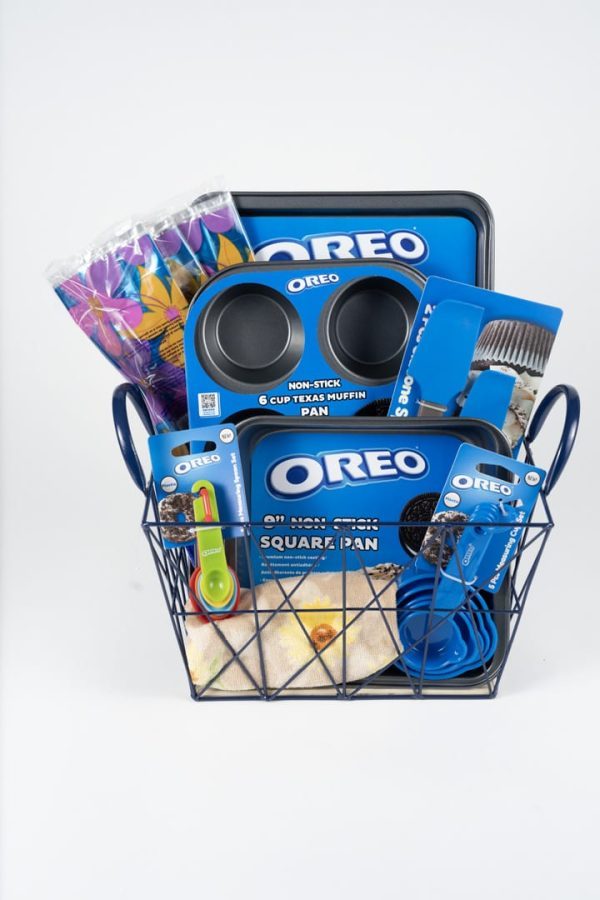 The "Everyday Baking" gift basket is filled with must-have baking essentials, including Oreo-themed items such as a 6-cup muffin pan, a square pan, a rubber spatula, and measuring spoons. Brightly colored paper cups and napkins provide a vibrant contrast to the plain white background they are presented against.