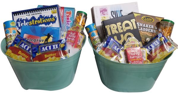 Two mint-green Automotive Baskets are filled with various board games, snacks, and popcorn packs. Visible games include "Telestrations," "Snakes and Ladders," "Pictionary," and "TelegraV." These baskets appear ready for a fun game night that will rev your excitement like an automotive engine.