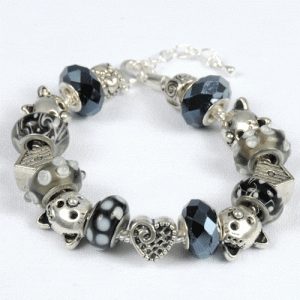 Introducing the Gray Tabby Bracelet: a stunning beaded accessory adorned with an assortment of patterned beads in elegant shades of black, white, gray, and silver. Featuring charming designs such as polka dots, stripes, and facets, some beads even include small ear-like protrusions. A beautifully detailed heart-shaped bead takes center stage in this exquisite piece.