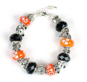 The Happy Halloween Bracelet showcases a distinctive alternating pattern of orange beads with white swirls, black faceted beads, and owl-shaped silver charms. This festive accessory is designed with a chain and clasp, arranged in a circular shape against a white background.