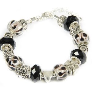 The Biker Girl Bracelet showcases alternating black and silver beads, detailed silver floral charms and a heart, and round milky white beads with black swirls. This edgy accessory is secured with a clasp and chain.