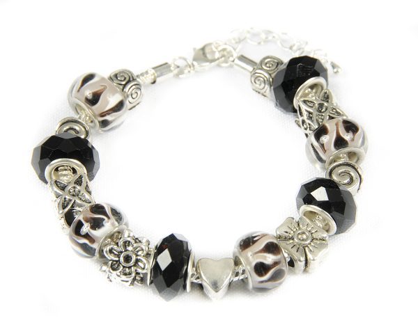 The Biker Girl Bracelet showcases alternating black and silver beads, detailed silver floral charms and a heart, and round milky white beads with black swirls. This edgy accessory is secured with a clasp and chain.