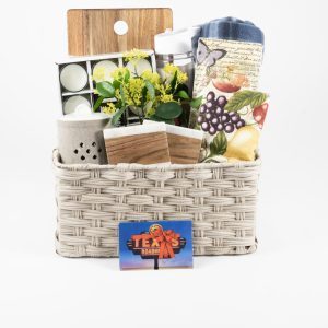 The "Kitchen & Home Large with $50 in Texas Roadhouse Certificates" features a woven basket containing a small plant, a set of tea lights, a kitchen cutting board, a fruit-print towel, a ceramic container, a wooden box, and a stainless steel tumbler. In front of the basket is also included a gift card for Texas Roadhouse worth $50.