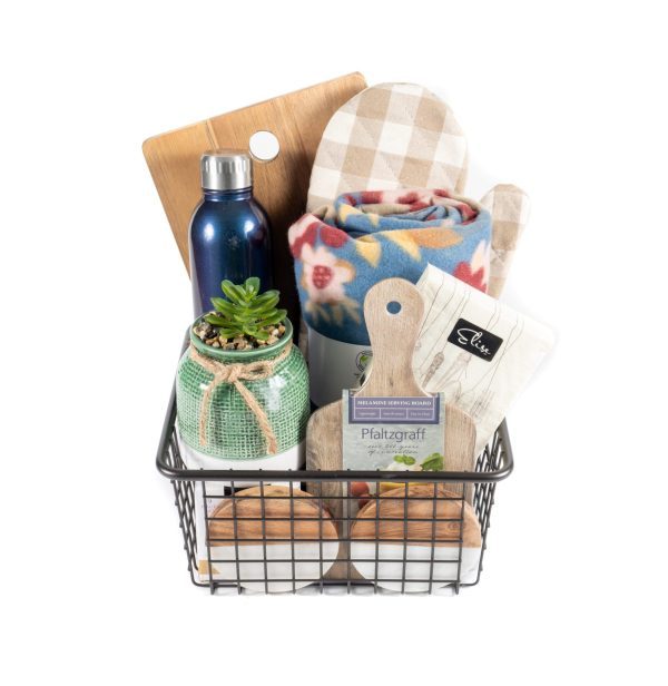 The "Kitchen & Home Medium" basket in black contains a variety of items, including a cutting board, a blue water bottle, a plaid oven mitt, a rolled-up blanket, a jar with a succulent, small kitchen tools, and tea packets. This medium-sized basket is beautifully arranged to present a rustic home kitchen gift set.