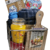 The Automotive Basket, filled with a yellow citrus candle, wooden cutting board, black water bottle, blue fleece blanket, wooden "HOME" sign with floral decor, and a heart-shaped floral pattern fabric item, is the perfect gift for automotive enthusiasts.