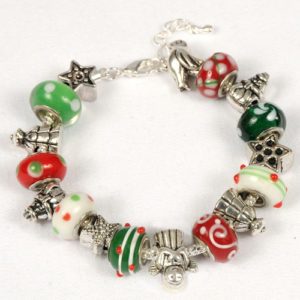 The Whimsical Christmas Bracelet boasts an array of festive, Christmas-themed beads in green, red, and white glass adorned with decorative patterns. It features silver charms shaped like Christmas trees, stars, and other holiday motifs. This charming piece of jewelry is finished with a metal clasp and arranged in a circular shape.