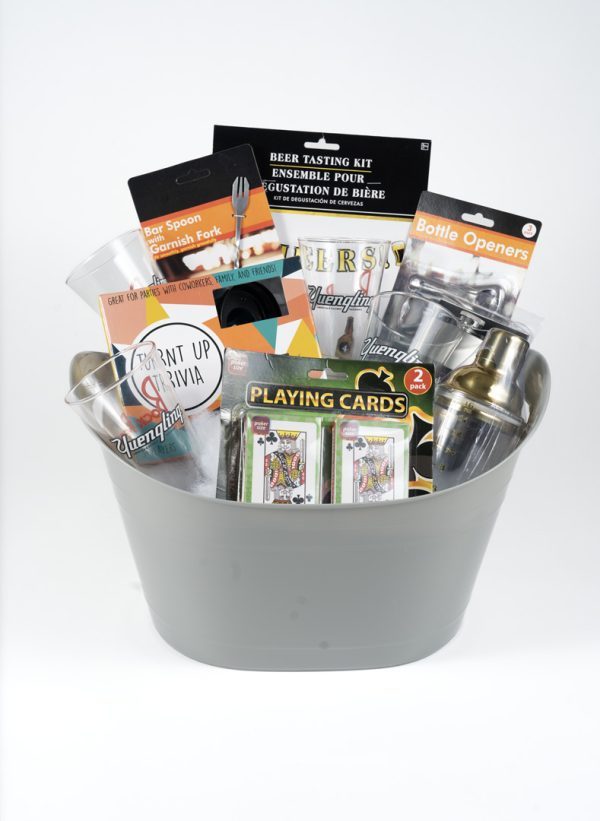 The Adult Game Night Basket features a gray bucket filled with an array of bar-themed items, including a beer tasting kit, a bar spoon and garnish fork, bottle openers, playing cards, drinking glasses, and a cocktail shaker—all set against a white background. It's the perfect addition to any adult game night.