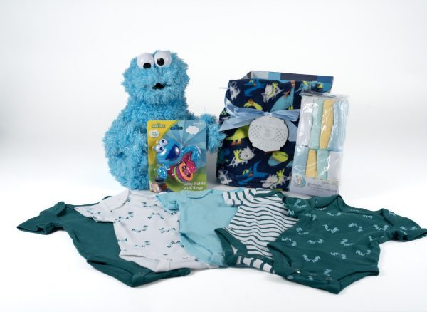 Displayed is the Adult Gambling Night Basket, which includes a blue Cookie Monster plush toy** for luck, baby clothes in shades of teal and white with various patterns **for cozy vibes**, a matching blanket **for comfort**, a pack of baby bath time essentials **to unwind after the game**, and a blue and green teething toy—all neatly arranged in this charming basket.