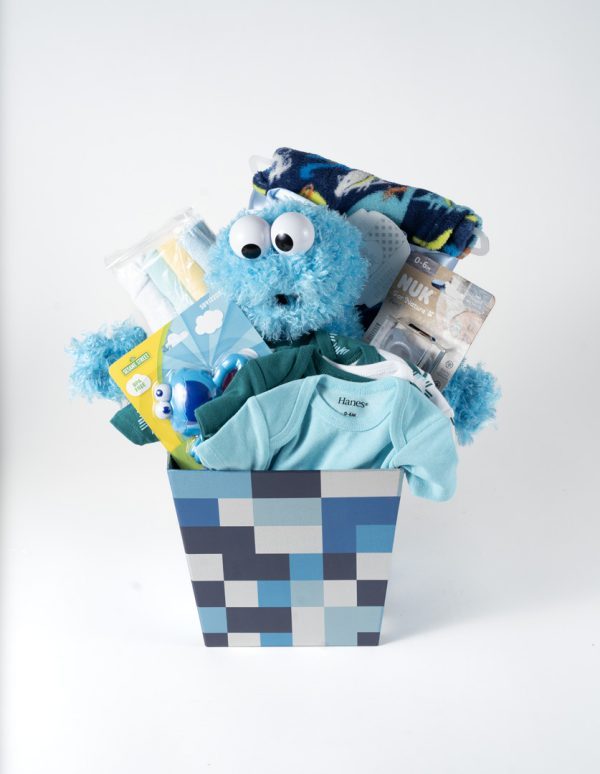 The Adult Gambling Night Basket contains a blue plush toy resembling a monster with googly eyes, a rolled-up blanket with animal prints, a set of baby pacifiers, baby bodysuits, a pair of socks, and a teething toy, all arranged in a blue and gray patterned container.