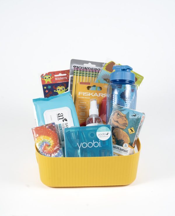 A yellow rectangular basket filled with assorted school supplies including a blue water bottle, a pack of Fiskars scissors, a set of colored markers, a packet of baby wipes, a pack of stickers, an adult notepad, hand sanitizer, and a tie-dye notebook has been renamed as the "Adult Gambling Night Basket.