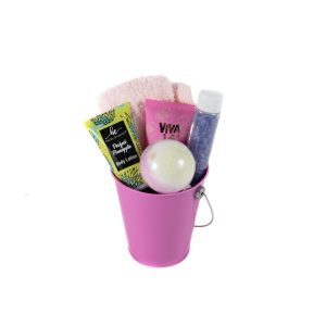 Introducing the ultimate Women’s Spa Bucket with Free Food Certificate: a pink metal container featuring a white bath bomb, a tube of body lotion, a pink washcloth, a VIVA-labelled pink bottle, and a clear plastic bottle filled with blue crystals. The bucket comes with a small metal handle and items are neatly arranged for your relaxation.