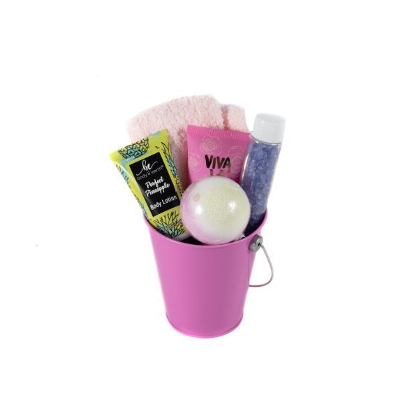 Introducing the ultimate Women’s Spa Bucket with Free Food Certificate: a pink metal container featuring a white bath bomb, a tube of body lotion, a pink washcloth, a VIVA-labelled pink bottle, and a clear plastic bottle filled with blue crystals. The bucket comes with a small metal handle and items are neatly arranged for your relaxation.