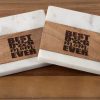 A Pair of Best Dog Mom Ever Square Coasters, featuring a design of light wood and white marble with each coaster engraved with the phrase "Best Dog Mom Ever" and a paw print replacing the "O" in "Dog," placed on a wooden surface.