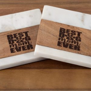 A Pair of Best Dog Mom Ever Square Coasters, featuring a design of light wood and white marble with each coaster engraved with the phrase "Best Dog Mom Ever" and a paw print replacing the "O" in "Dog," placed on a wooden surface.