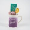 The "You are Blessed Mug Gift Basket with Free Food Certificate" features a stunning white and purple gradient Blessed Mug inscribed with "You are Blessed." Inside, you'll find a small green plaque reading "Grateful," along with a pink and purple plush toy and a honey lollipop wrapped in plastic. This delightful ensemble is showcased against a plain background, creating an exquisite gift basket.