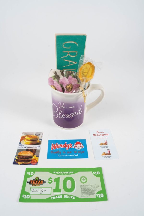 A "You are Blessed Mug Gift Basket with Free Food Certificate" includes a purple ceramic mug featuring "You are Blessed" written on it. Inside the mug, you'll find a green sign with "Grateful," a lollipop, and floral-themed socks. Surrounding the mug is a $10 Texas Roadhouse voucher, along with gift cards from Wendy's, McDonald's, and Chick-fil-A.