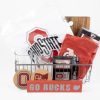 The personalized Buckeye Basket features a variety of Ohio State University items, such as a white T-shirt with the OSU logo, custom glasses, coasters, a small red pennant, and a personalized cutting board. Displayed in front of the basket is a block sign that reads "GO BUCKS".