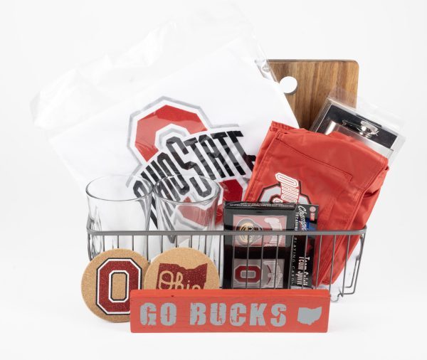 The personalized Buckeye Basket features a variety of Ohio State University items, such as a white T-shirt with the OSU logo, custom glasses, coasters, a small red pennant, and a personalized cutting board. Displayed in front of the basket is a block sign that reads "GO BUCKS".