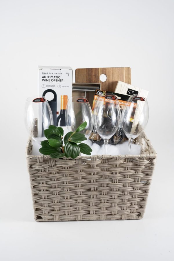 The Celebration Basket with 4 Riedel Glasses - JUST ADD WINE includes four empty Riedel glasses, a plant, an automatic wine opener, a wooden cutting board, a cheese slicer, and two packaged items with partially visible labels. The background is plain white.