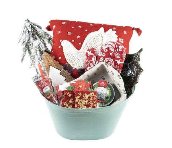 The Christmas Home & Kitchen Gift Basket - Premium is the perfect holiday offering, featuring a variety of festive items such as a red pillow adorned with a white bird design, a small evergreen tree, red and gold gift boxes, candles, a ceramic dish, and a decorative plate shaped like a holly leaf—all beautifully arranged in an elegant blue container to enhance your home and kitchen décor.