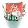 The "Christmas Home & Kitchen Gift Basket - Premium" includes a red pillow adorned with an embroidered Christmas tree, a rolling pin, two green mugs featuring white tree designs, pine-scented candles, a festive plate, and various other holiday-themed items, all beautifully arranged in a green bucket.