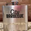 A sleek, silver flask with a screw-on cap rests on a speckled countertop. Adorned with the "City Barbeque" logo in bold, black lettering, this Silver Flask - Your Custom Text/Logo Here stands out. The background features a tiled wall.