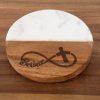 A round coaster named "Believe - Round" sitting on a wooden surface. The coaster features a design that is half white marble and half brown wood, with an infinity symbol and cross engraved on the wooden part. The word "Believe" is stylishly integrated into the infinity symbol.