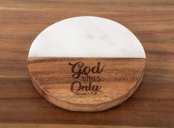 The "God Vibes Only - Round" coaster, made of wood and marble, sits elegantly on a wooden surface. This beautifully balanced piece features half wood and half white marble, with the text "God Vibes Only" engraved on the wooden portion.