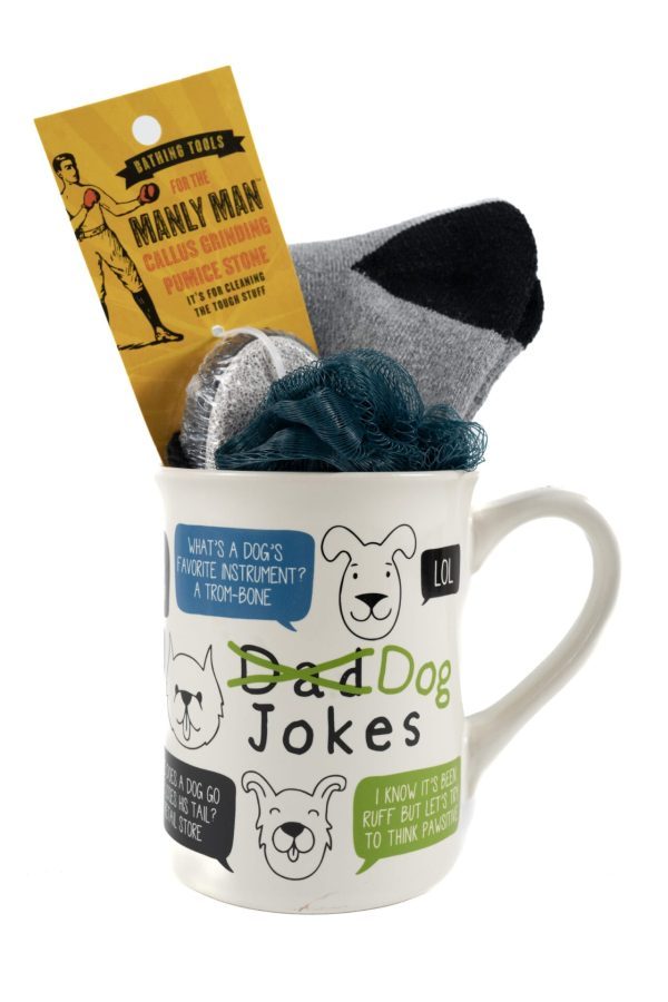 The Dog Jokes Mug Gift Basket with Free Food Certificate features a blue loofah, gray socks, a Free Food Certificate, and a yellow package labeled "Manly Man Callus Grinder." The mug showcases a cartoon dog face along with text bubbles containing corny dog-themed dad jokes.