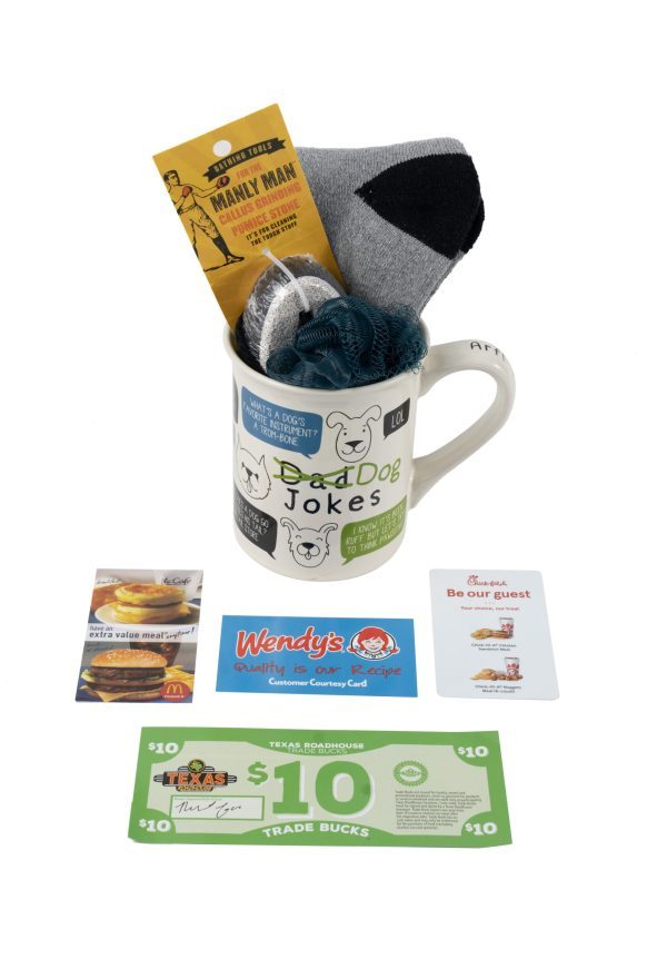 The Dog Jokes Mug Gift Basket with Free Food Certificate includes a ceramic mug filled with socks, a pumice stone, and a "Manly Man" grooming product. Accompanying the mug are three gift cards for McDonald's, Wendy's, and Chick-fil-A, as well as a $10 Texas Roadhouse free food certificate. It's the ultimate gift basket for any man!