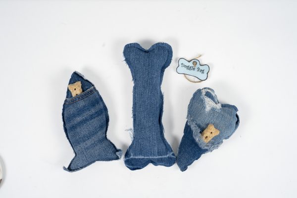 Three denim dog toys are arranged on a white background. The toys, shaped like a fish, bone, and heart, each come with a small treat or chew piece and some distressed denim elements. Perfect for keeping your adult dog's night fun and engaging. There is also a hanging tag labeled "Adult Gambling Night Basket.