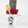 An Everyday Hero Mug Gift Basket that includes a whimsical white mug featuring a figure holding a red piece of fabric, accompanied by a honey lollipop, and a card inscribed with "believe" in gold lettering. Perfect for giving on its own or paired with the free food certificate to make it an extra special gift for someone you cherish.