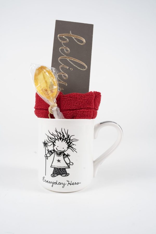 An Everyday Hero Mug Gift Basket that includes a whimsical white mug featuring a figure holding a red piece of fabric, accompanied by a honey lollipop, and a card inscribed with "believe" in gold lettering. Perfect for giving on its own or paired with the free food certificate to make it an extra special gift for someone you cherish.