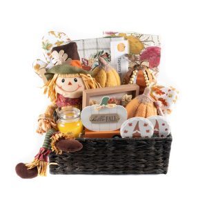 The Fall Harvest Gift Basket - Large perfectly captures the essence of autumn with its scarecrow doll, bright yellow candle, plush pumpkins, pumpkin-themed greeting card, and various autumn-decorated kitchen linens—all beautifully arranged in a dark wicker basket.