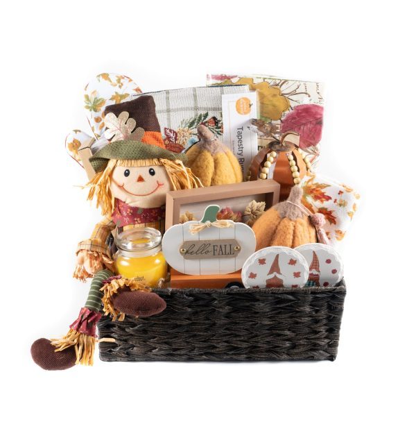 The Fall Harvest Gift Basket - Large perfectly captures the essence of autumn with its scarecrow doll, bright yellow candle, plush pumpkins, pumpkin-themed greeting card, and various autumn-decorated kitchen linens—all beautifully arranged in a dark wicker basket.