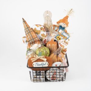 The Fall Harvest Gift Basket - Medium is filled with various items including pumpkins, a "Thankful" sign, autumn leaves, a plaid napkin, a scarecrow, a mini cutting board, and sunflower accents. This delightful gift basket celebrates the fall harvest season and Thanksgiving.