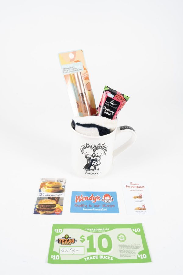 The Friends Mug Gift Basket With Free Food Certificate features a black and white Friends Mug holding a makeup brush set and a tube of lip gloss. Included below the mug are a $10 Wendy's gift card, a McDonald’s coupon, and what looks like $10 in trade bucks, completing this eclectic gift basket set against a white background.