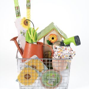 A wire basket holds a variety of brightly colored Adult Gambling Night Basket items, including a green garden hose nozzle, a birdhouse, gloves, a watering can, a floral kneeling pad, flower seeds, and a roll of garden twine. These items are neatly arranged in the basket—ideal for an adult's weekend gardening escape.