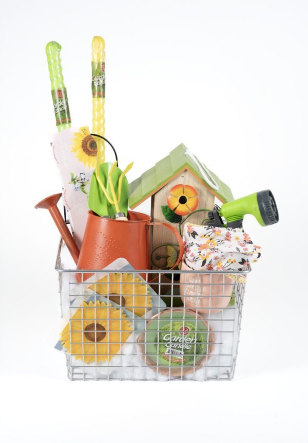 A wire basket holds a variety of brightly colored Adult Gambling Night Basket items, including a green garden hose nozzle, a birdhouse, gloves, a watering can, a floral kneeling pad, flower seeds, and a roll of garden twine. These items are neatly arranged in the basket—ideal for an adult's weekend gardening escape.