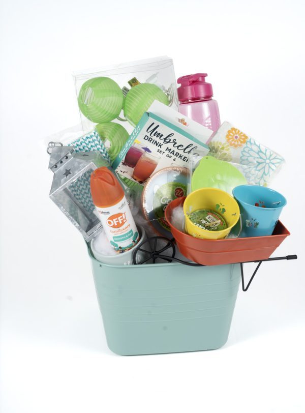 The Adult Gambling Night Basket is filled with assorted items, including a pink water bottle, green and blue paper lanterns, OFF! insect repellent, a lantern-shaped candle holder, gardening gloves, small flower pots, a yard game set, and a package labeled "Umbrella Drink Markers.