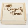 The "Gift Box - Congratulations Grad" is a wooden gift box featuring a sliding lid engraved with the words "Congrats Grad" beneath an intricately detailed graduation cap. This elegant box, ideal for celebrating such a significant achievement, is showcased against a pristine white background.