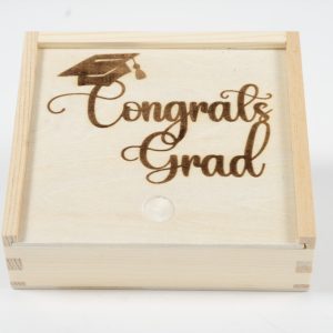 The "Gift Box - Congratulations Grad" is a wooden gift box featuring a sliding lid engraved with the words "Congrats Grad" beneath an intricately detailed graduation cap. This elegant box, ideal for celebrating such a significant achievement, is showcased against a pristine white background.