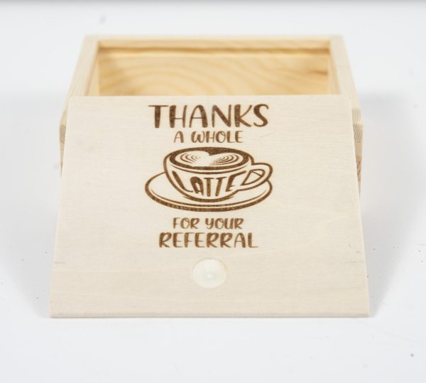 A small, wooden gift box called "Gift Box - Thanks a Whole Latte for your Referral" with an open lid. The lid rests against the box and features an engraving of a coffee cup with latte art. Above the cup, the text reads "THANKS A WHOLE LATTE," and below it says "FOR YOUR REFERRAL." This charming keepsake makes for a thoughtful referral thank you.