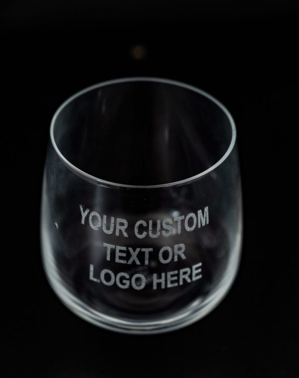 A clear, empty glass from the Pair of Rocks/Juice Glasses collection with the text "YOUR CUSTOM TEXT OR LOGO HERE" etched in white on its surface. The glass, ideal for juice, is set against a dark background.